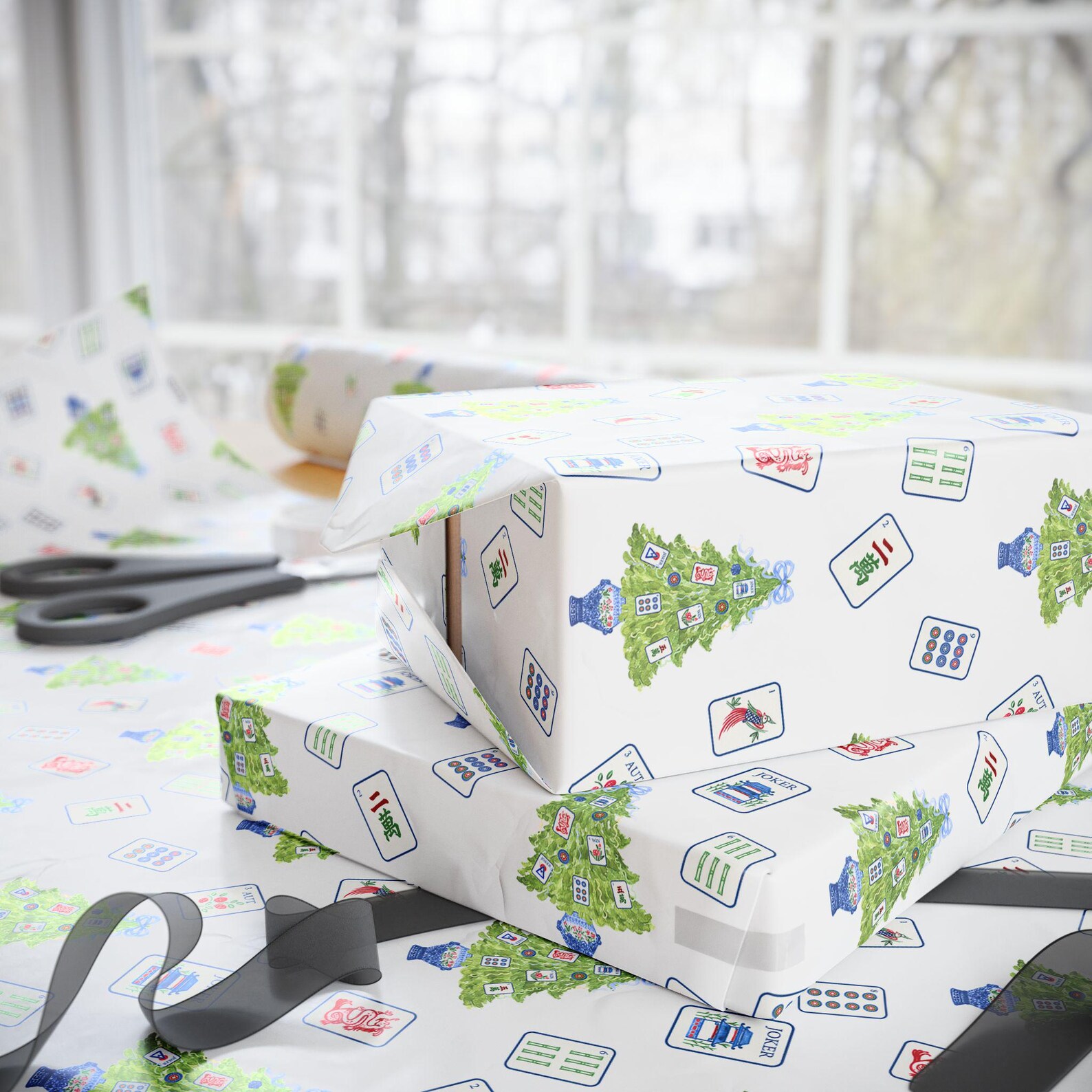 Stacked gifts wrapped in white Mahjong Christmas paper on a bright wrapping table
